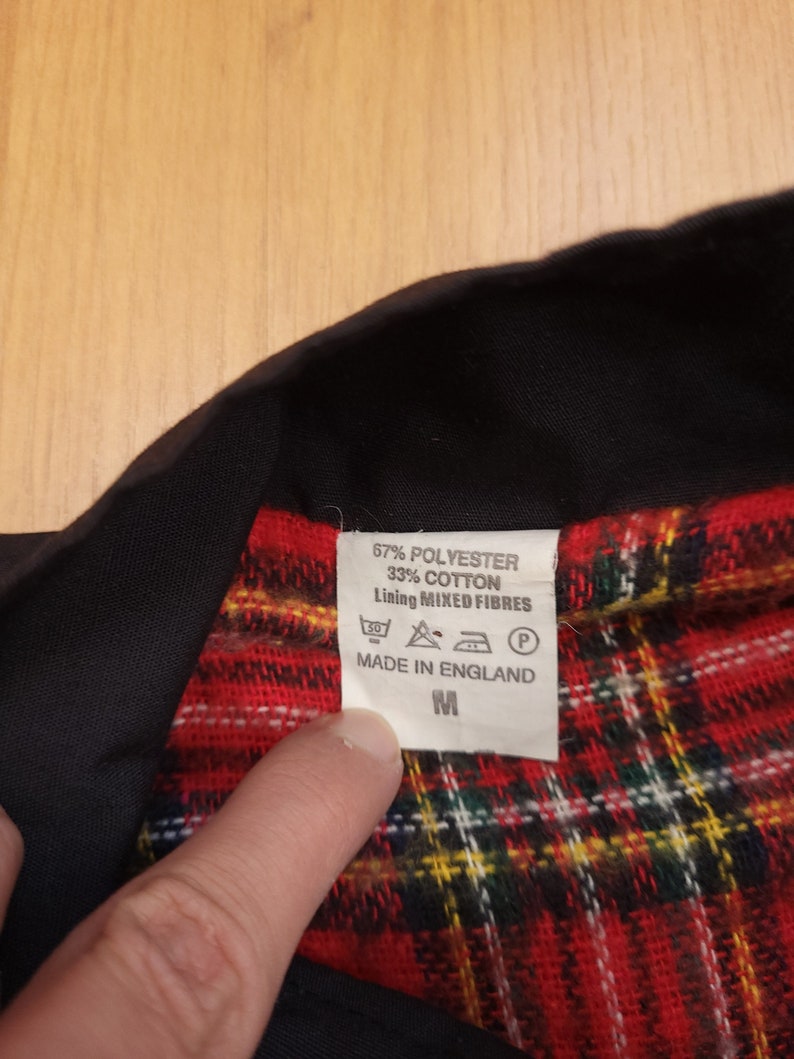 Peut inclure: Une chemise &agrave; carreaux noirs et rouges avec un col noir et une &eacute;tiquette blanche indiquant "67% Polyester 33% Coton Doublure Fibres Mixtes" et "Fabriqu&eacute; en Angleterre". L'&eacute;tiquette indique &eacute;galement la taille "M".