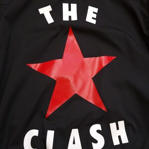 Peut inclure: Veste noire avec une &eacute;toile rouge et les mots "THE CLASH" en blanc.