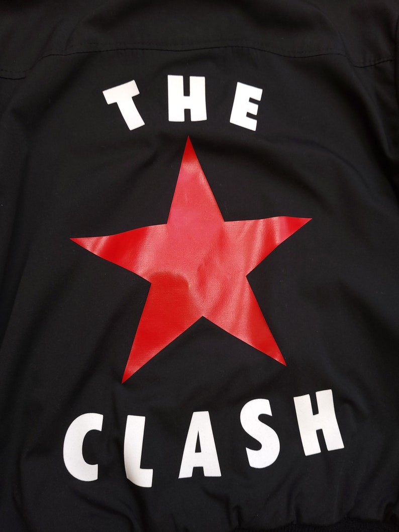 Peut inclure: Veste noire avec une &eacute;toile rouge et les mots "THE CLASH" en blanc.