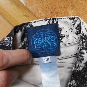 May include: Close-up of a pair of jeans with a black and white pattern. The blue label reads "KENZO JEANS" and the size tag shows "36". The jeans are made of a light-coloured fabric.