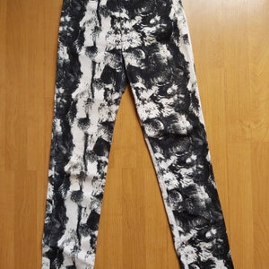 May include: High-waisted denim jeans featuring a black and white abstract pattern. The jeans have a classic five-pocket design and a button and zip closure. The pattern resembles a textured, fur-like design.