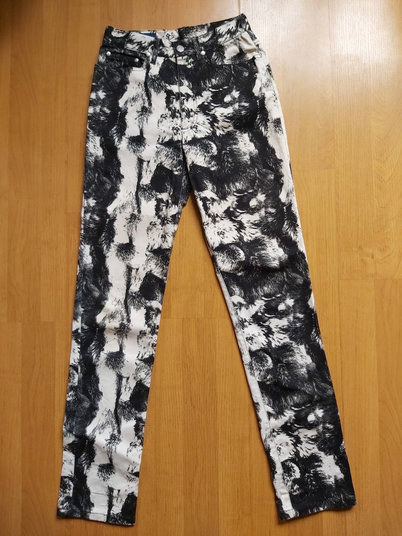 May include: High-waisted denim jeans featuring a black and white abstract pattern. The jeans have a classic five-pocket design and a button and zip closure. The pattern resembles a textured, fur-like design.