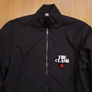 Peut inclure: Une veste bomber noire avec une fermeture &eacute;clair et un patch blanc "The Clash" avec une &eacute;toile rouge.