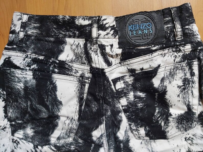 May include: The rear view of high-waisted jeans with a striking black and white pattern. The jeans feature two back pockets and a leather patch with the "KENZO JEANS" logo. The pattern is abstract.