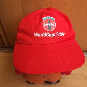 May include: Red baseball cap with a white Coca-Cola logo and the text "World Cup USA 94" in white.