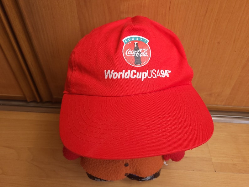 May include: Red baseball cap with a white Coca-Cola logo and the text "World Cup USA 94" in white.