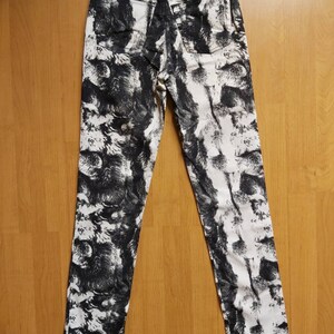 May include: High-waisted jeans with a black and white abstract pattern. The jeans have a classic five-pocket design and a leather patch with text on the back. The fabric is a medium weight denim.