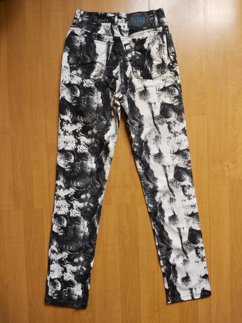May include: High-waisted jeans with a black and white abstract pattern. The jeans have a classic five-pocket design and a leather patch with text on the back. The fabric is a medium weight denim.
