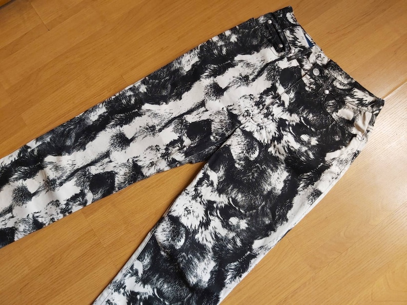 May include: Black and white patterned jeans. The design features a repeating pattern of black brushstrokes on a white background. The jeans have a classic five-pocket design and a button and zip closure.