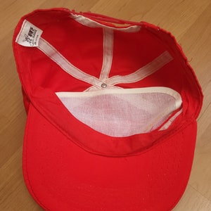 May include: Red baseball cap with a white mesh lining and a white label that says "LEVIS 100% COTTON MADE IN TAIWAN".