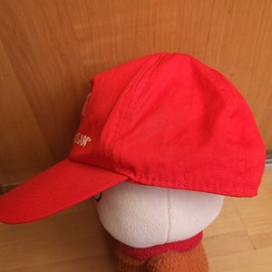 May include: A red baseball cap with a white embroidered logo. The logo says "Nissan".