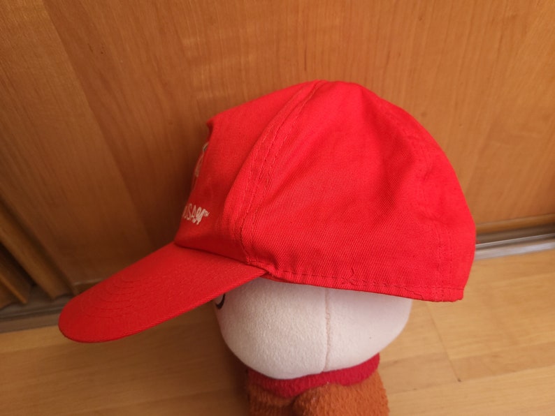 May include: A red baseball cap with a white embroidered logo. The logo says "Nissan".