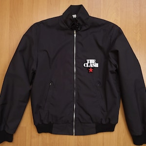 Peut inclure: Une veste bomber noire avec une fermeture &eacute;clair et un patch &eacute;toile rouge avec le texte "THE CLASH" en blanc.