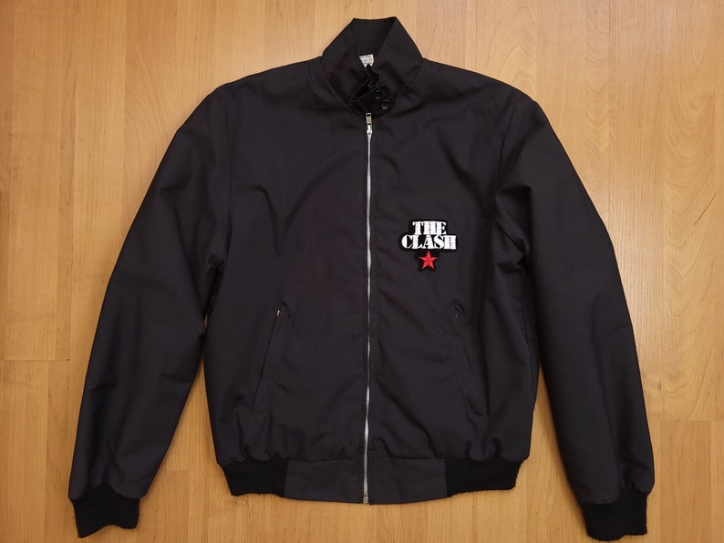 Peut inclure: Une veste bomber noire avec une fermeture &eacute;clair et un patch &eacute;toile rouge avec le texte "THE CLASH" en blanc.