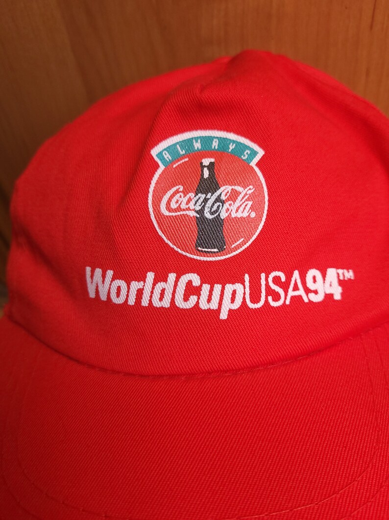 May include: Red baseball cap with a white Coca-Cola logo and the text "Always Coca-Cola World Cup USA 94" embroidered on the front.