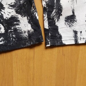 May include: Detail of the hem of trousers featuring a black and white abstract design. The fabric has a textured look, with the black pattern resembling brushstrokes or animal fur.