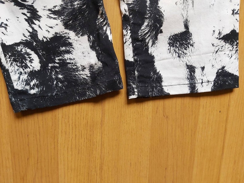 May include: Detail of the hem of trousers featuring a black and white abstract design. The fabric has a textured look, with the black pattern resembling brushstrokes or animal fur.