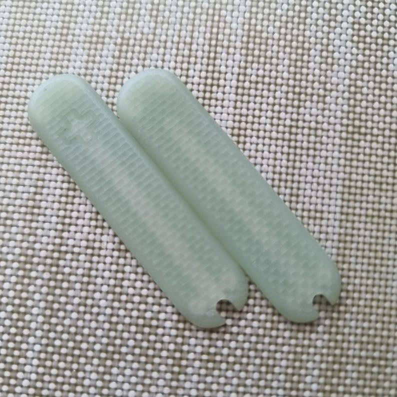 Puede incluir: Dos objetos rectangulares de color verde p&aacute;lido con extremos redondeados y una superficie texturizada. Un extremo de cada objeto tiene un peque&ntilde;o recorte semicircular. Los objetos est&aacute;n sobre una superficie texturizada blanquecina.