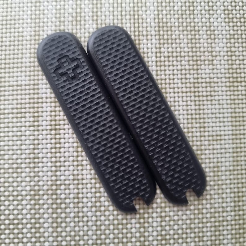 Puede incluir: Dos cachas negras de repuesto para una navaja de bolsillo. Las cachas tienen un patr&oacute;n texturizado en forma de rejilla y un emblema de cruz. Las cachas miden aproximadamente 9 cm de largo.