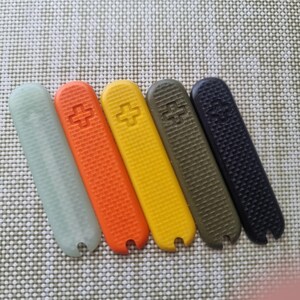 Puede incluir: Una colecci&oacute;n de cinco cachas multicolores para navaja suiza. Los colores son verde claro, naranja, amarillo, verde oliva y negro. Cada cacha tiene una superficie texturizada y un emblema de cruz.
