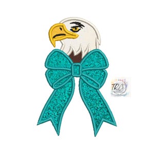 May include: An embroidered design of a bald eagle wearing a teal blue bow. The eagle has a white head and brown eyes. The bow is tied with a large, fluffy knot.