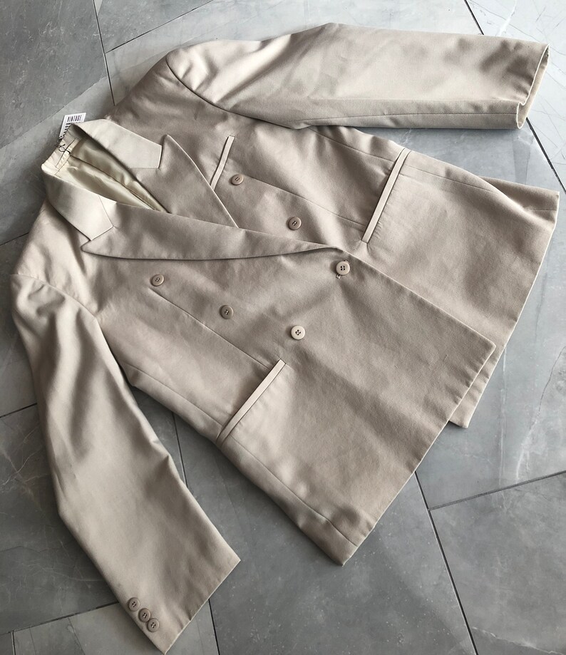 Puede incluir: Un blazer beige de doble botonadura con un dise&ntilde;o cl&aacute;sico. El blazer presenta solapas con muescas, dos filas de botones y dos bolsillos delanteros. Las mangas tienen botones en los pu&ntilde;os. La prenda est&aacute; hecha de una tela suave y es adecuada para varias ocasiones.