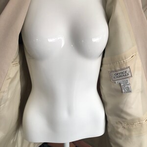Puede incluir: Blazer beige con bolsillos interiores y una etiqueta que dice "OFFICE CASUALS". El blazer se muestra en un maniqu&iacute; blanco. El forro interior es de color beige claro.