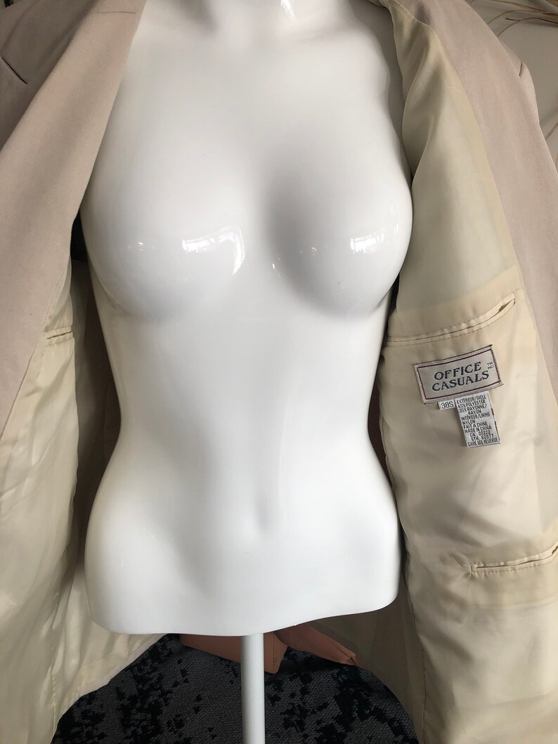 Puede incluir: Blazer beige con bolsillos interiores y una etiqueta que dice "OFFICE CASUALS". El blazer se muestra en un maniqu&iacute; blanco. El forro interior es de color beige claro.
