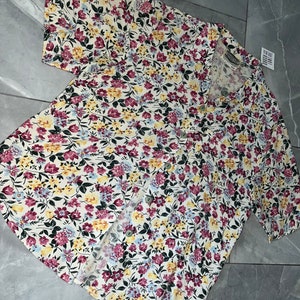 Peut inclure: Une chemise boutonnée blanche à imprimé floral dans les tons jaune, rose et bleu. La chemise a des manches courtes et un col.