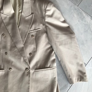 Puede incluir: Un blazer beige de doble botonadura con cuatro botones y dos bolsillos delanteros. El blazer tiene solapas con muescas y un corte entallado. Las mangas son largas y terminan en la mu&ntilde;eca. El blazer est&aacute; hecho de una tela lisa.