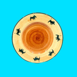 May include: A round, wooden plate with a light brown center and a darker brown rim. The plate features black silhouette illustrations of animals around the edge. The plate is set against a bright blue background.