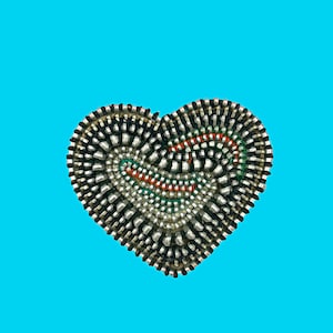May include: A heart-shaped item crafted from zippers, predominantly silver and black, with red, green, and white detailing. The background is a vibrant, bright blue.