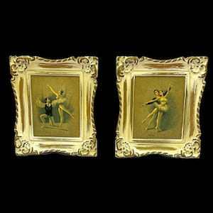 May include: A pair of framed vintage ballet prints. Each print depicts ballet dancers. The frames have an ornate design with a distressed white and gold finish. The background is black.