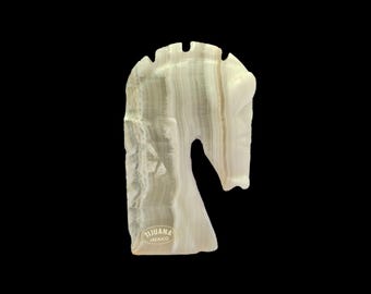 May include: A carved white onyx chess piece in the shape of a horse, with a textured surface and a natural, layered appearance. The piece has a stylized mane and a curved neck. The text "TIJUANA MEXICO" is visible.