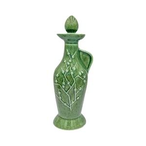 May include: A green ceramic bottle with a floral design and a lid. The bottle has a handle and a wide base.