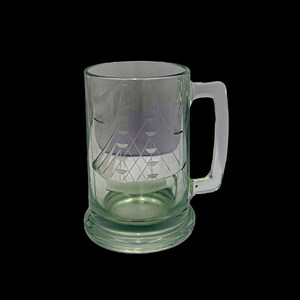 May include: A clear glass beer mug with a handle and a decorative etched design. The mug has a wide base and a cylindrical body. The etched design features geometric shapes. The mug is empty and sits against a black background.