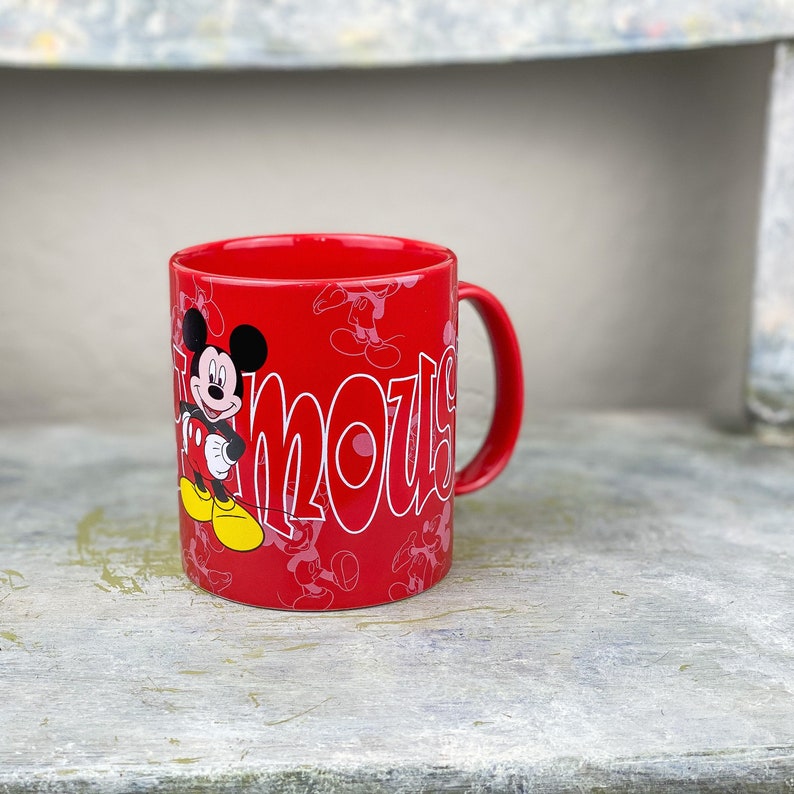 Pu&ograve; includere: Tazza in ceramica rossa con un contorno bianco di Topolino e la parola "mous" stampata su di essa.