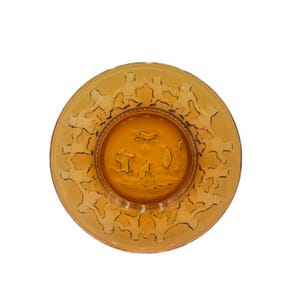 May include: Amber-colored glass plate with a detailed rim design and a central embossed scene. The plate features a circular shape with a raised rim and a detailed embossed design around the edge. The center of the plate has an embossed scene.