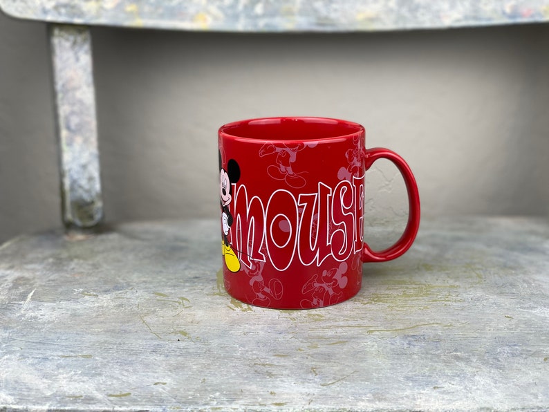 Pu&ograve; includere: Tazza in ceramica rossa con un contorno bianco di Topolino e la parola "Mouse" sul davanti. La tazza &egrave; decorata con un motivo di silhouette di Topolino.