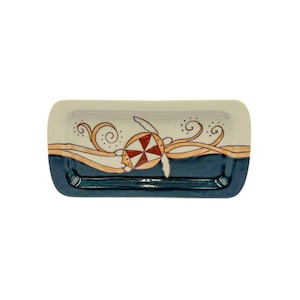 May include: A white ceramic serving dish with a blue rim and a hand-painted design of a sea turtle swimming in a wave. The turtle is orange, red, and yellow.