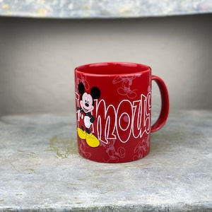 Pu&ograve; includere: Tazza in ceramica rossa con un design di Topolino. La tazza presenta Topolino nella sua posa caratteristica con la parola "Famous" scritta in un font stilizzato.