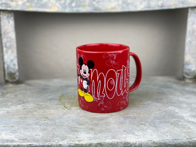 Pu&ograve; includere: Tazza in ceramica rossa con un design di Topolino. La tazza presenta Topolino nella sua posa caratteristica con la parola "Famous" scritta in un font stilizzato.