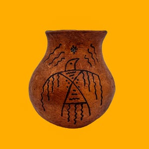 May include: A small, brown pottery vase with a wide opening. The vase is decorated with a black, stylized bird design, wavy lines, and a star-like symbol near the rim. The background is a bright yellow.