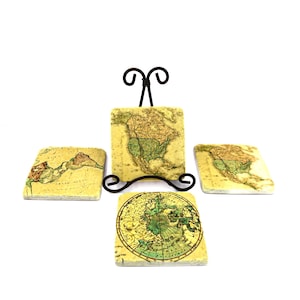May include: A set of four square coasters with antique map designs. One coaster is displayed on a black metal stand. The coasters feature a cream-colored background with green, brown, and yellow map details.