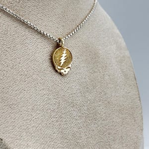 May include: A gold-toned pendant necklace with a silver chain. The pendant features a skull with a lightning bolt design.