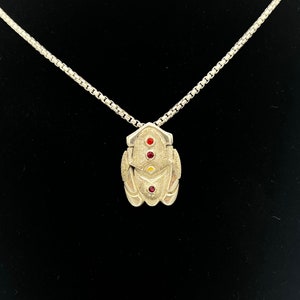 May include: A silver pendant necklace with a geometric design featuring three red and one yellow gemstones. The pendant is attached to a silver chain.