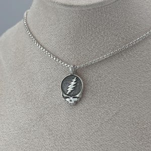May include: A silver chain necklace with a silver pendant featuring a skull with a lightning bolt inside.
