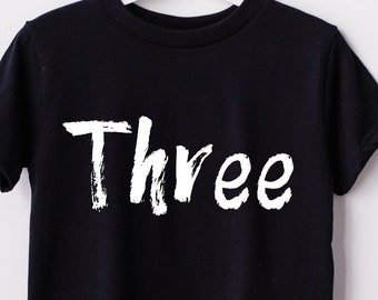 Könnte beinhalten: Schwarzes T-Shirt mit weißem Text "Three" in einer Pinselstrichschrift.
