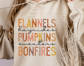 May include: A beige hoodie with the text "FLANNELS hayrides PUMPKINS sweaters BONFIRES" in a colourful, layered font.