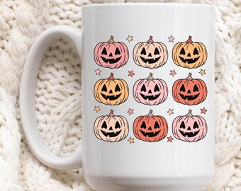 May include: White ceramic mug with a design of nine orange, pink, and peach jack-o'-lantern faces with stars.